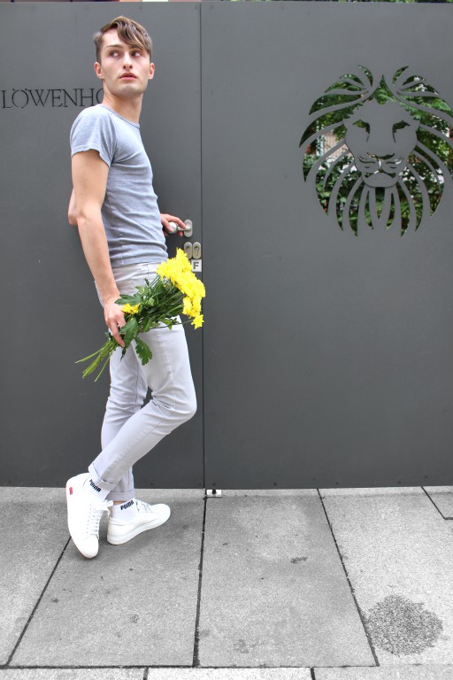 graues T-Shirt kombinieren - Junge mit gelben Blumen vor einem Tor - graues Outfit von Mister Matthew