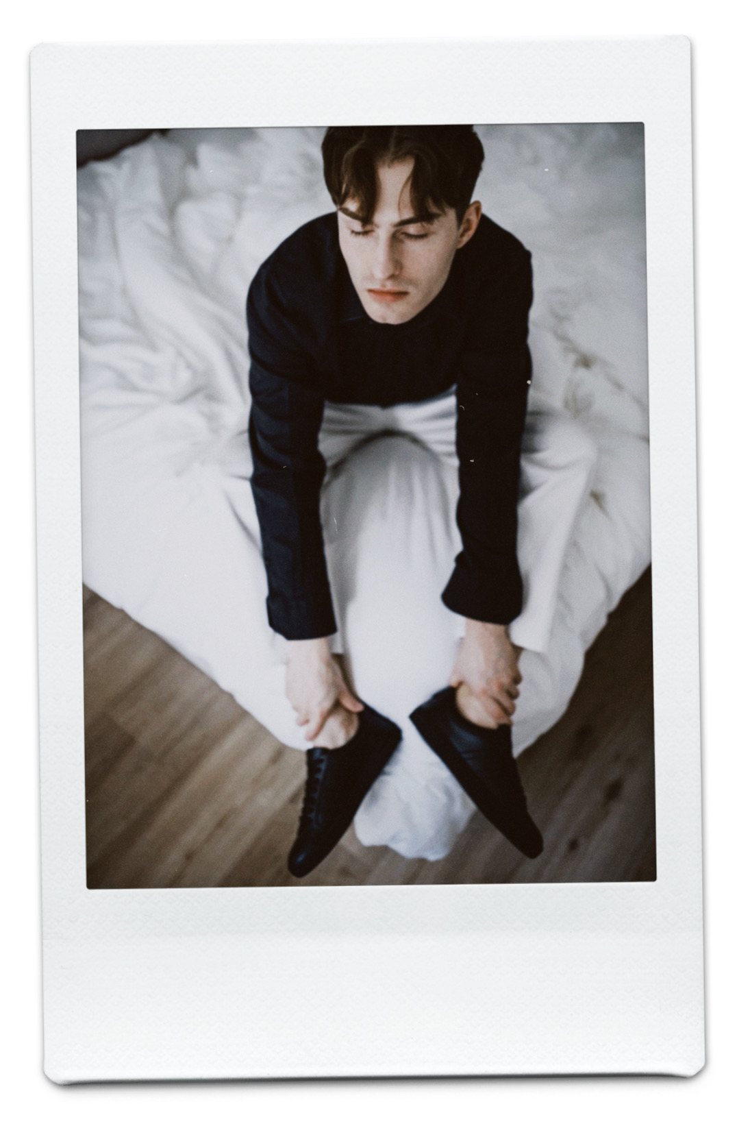 Mister Matthew Outfit in Schwarz-Weiß auf dem Bett sitzend.